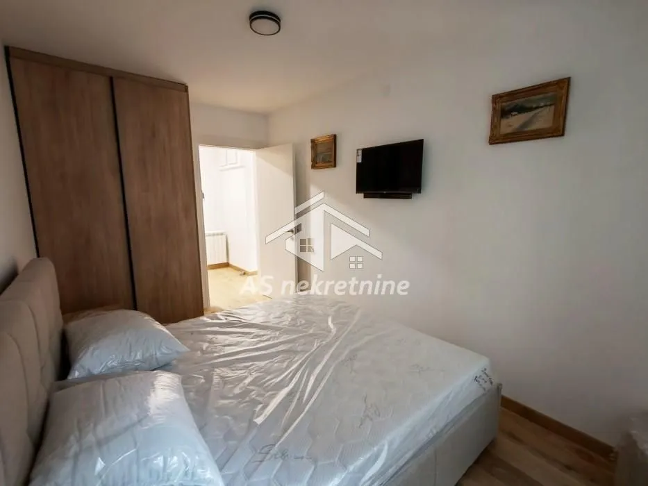 Furnished bedroom with a double bed, wardrobe, and wall-mounted TV.