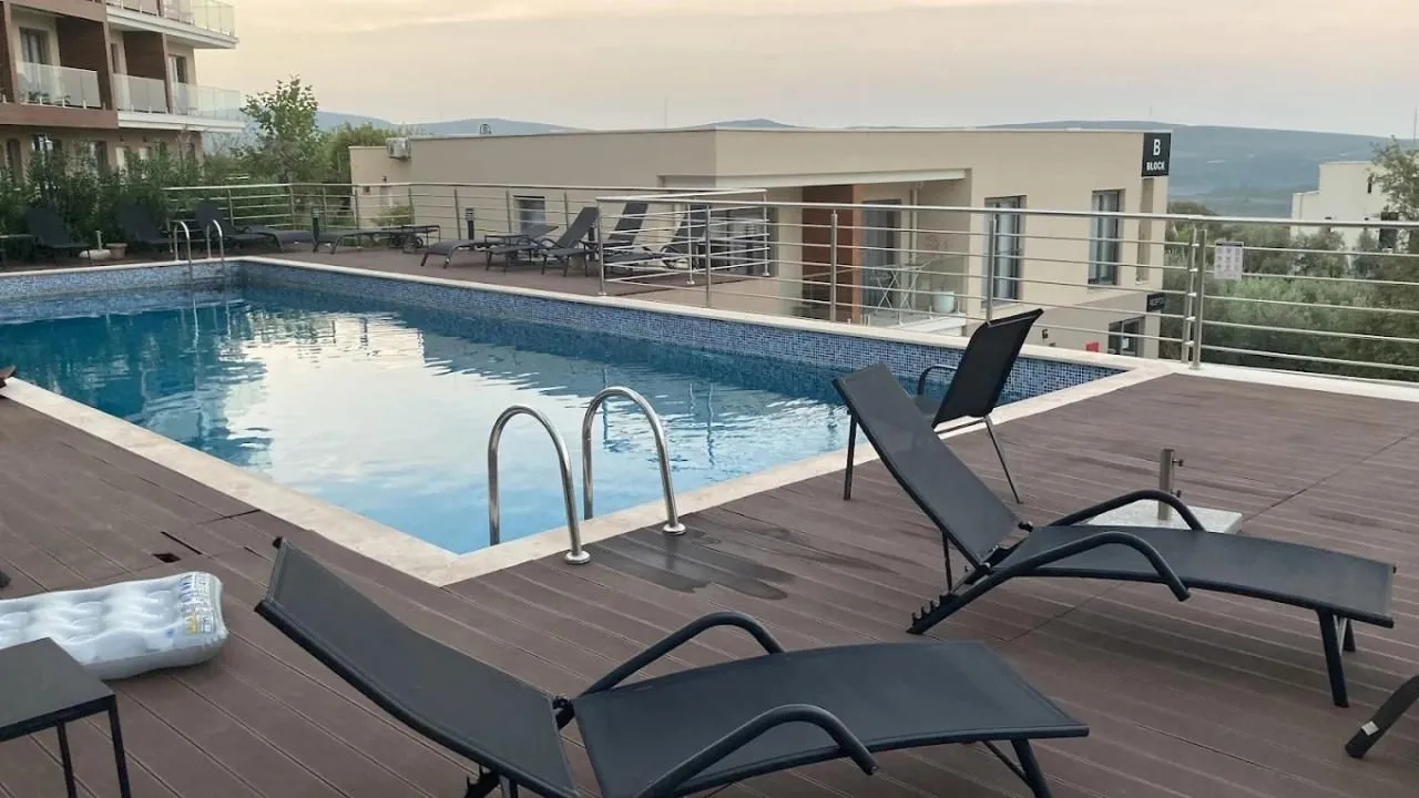Swimming pool with a wooden sun deck and loungers in front of the apartment building.