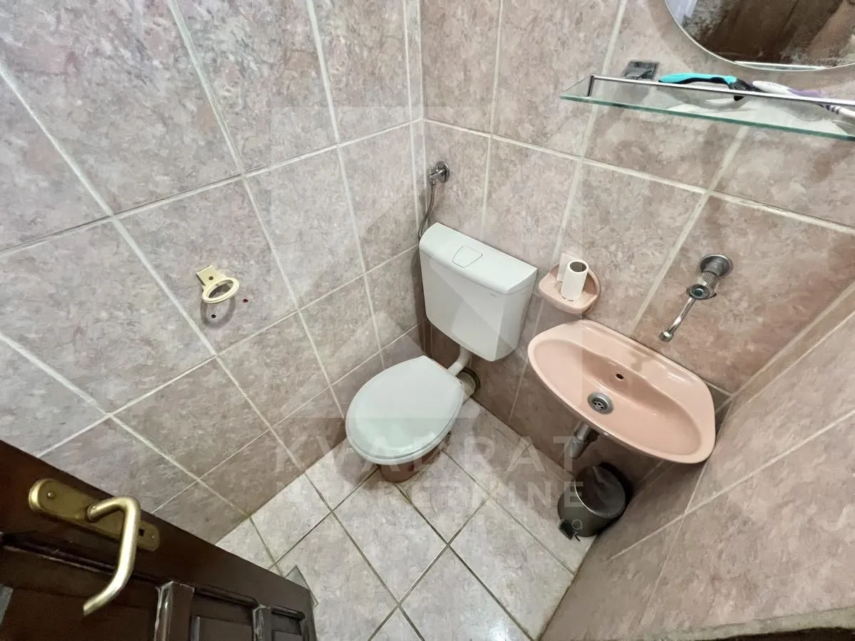 Smaller bathroom with a toilet and a sink, tiled with ceramic tiles.