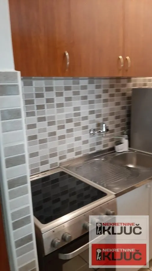 Manja kuhinja sa šporetom, sudoperom i drvenim visećim elementima.