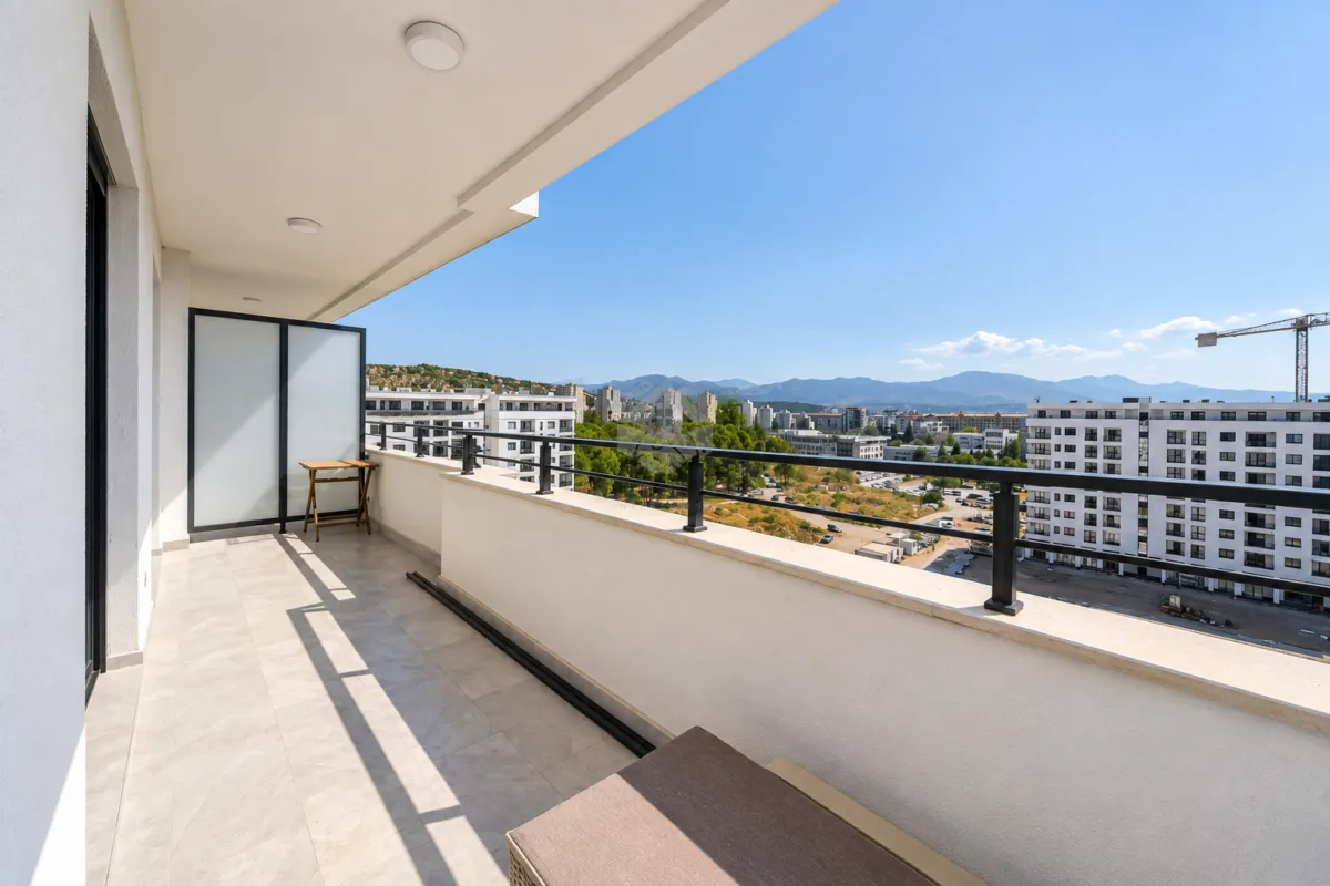 Prostrani popločani balkon sa ogradom i pogledom na grad i okolne planine.