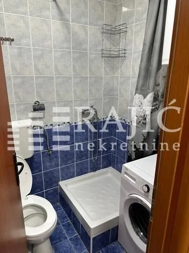 Small bathroom with blue tiles, shower cabin, toilet, and washing machine.