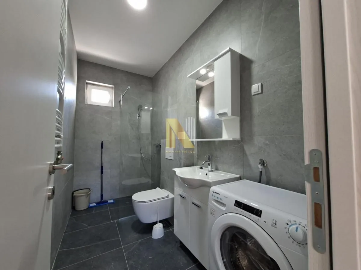 Modern bathroom with grey tiles, a walk-in shower, washbasin, and washing machine.
