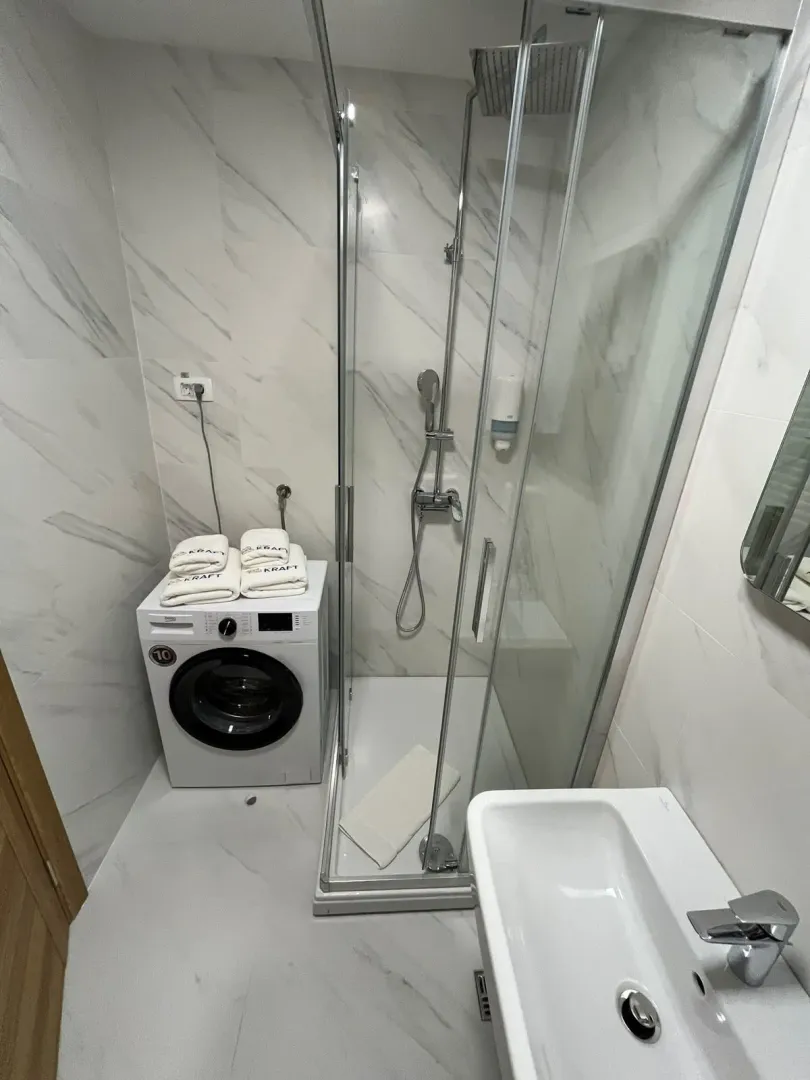 Moderne kupatilo sa tuš kabinom, umivaonikom i mašinom za veš.