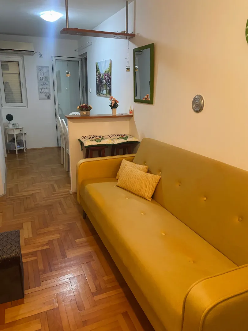 Living room with a yellow sofa and parquet flooring.
