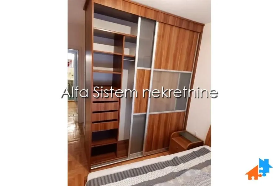 Spavaća soba sa velikim drvenim garderoberom sa kliznim vratima i otvorenim policama.