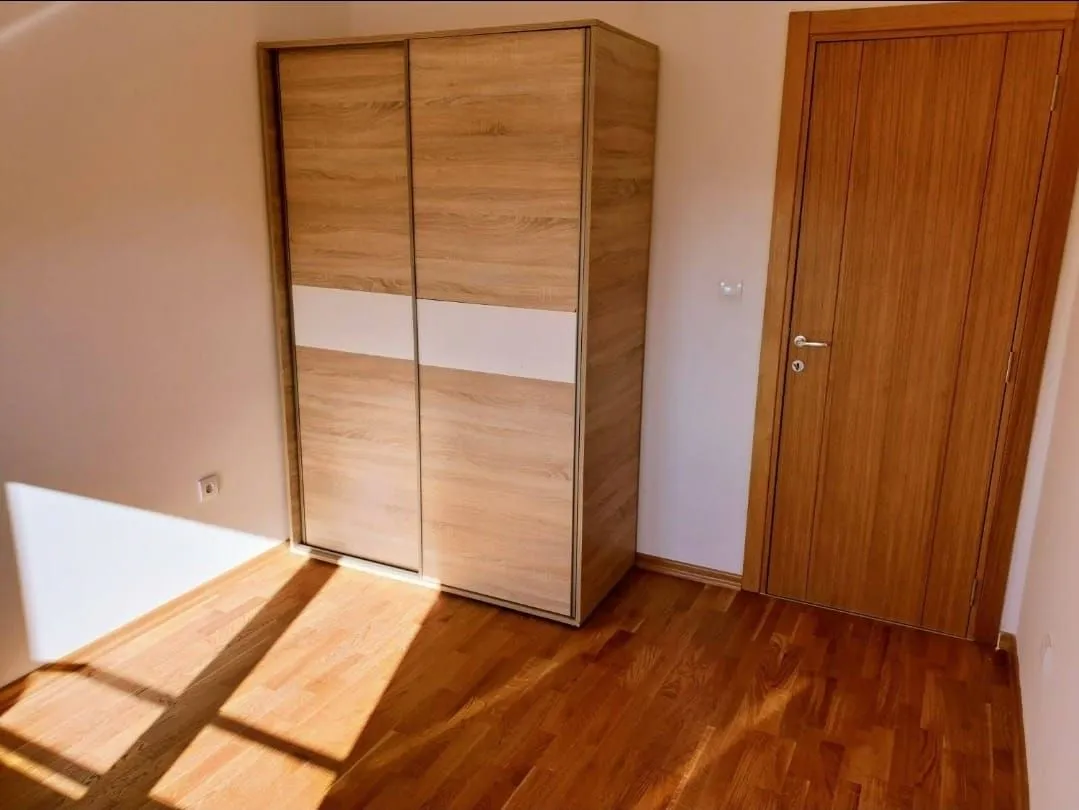 Manja spavaća soba sa drvenim garderoberom i laminatom na podu.