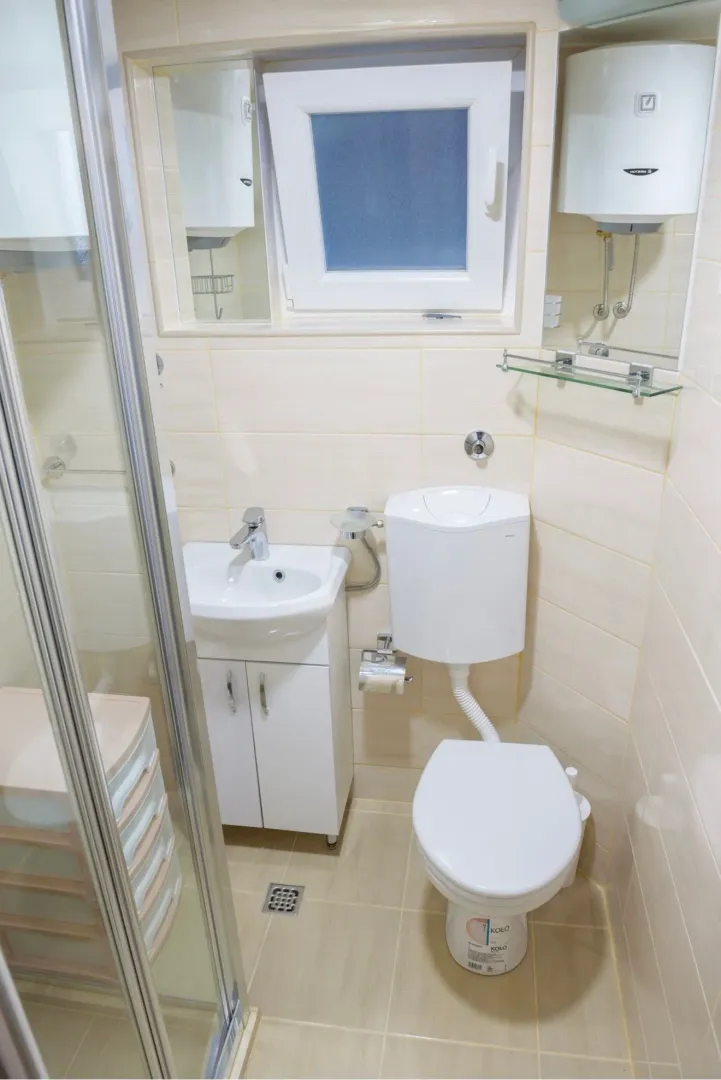 Smaller bathroom with a shower cabin, washbasin, and toilet in light tiles.