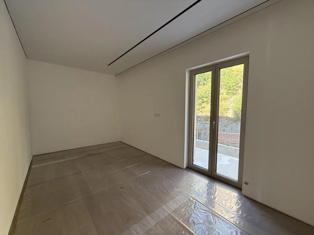 Prazna neopremljena soba sa balkonskim vratima i podom prekrivenim zaštitnom folijom.