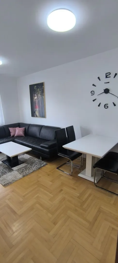 Bright living room with a black corner sofa and a dining table.