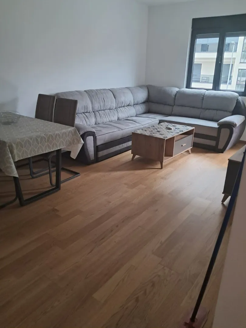 Dnevna soba sa ugaonom garniturom, trpezarijskim stolom i parketom.