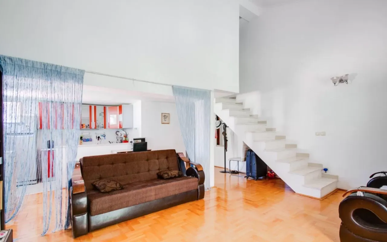 Living room with a brown sofa, staircase, and a view of the kitchen in the background.