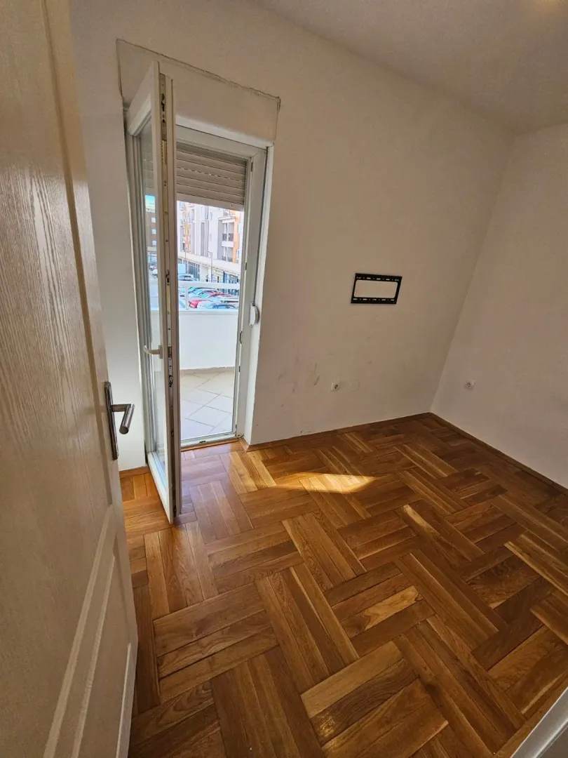 Empty room with hardwood parquet flooring and balcony access.