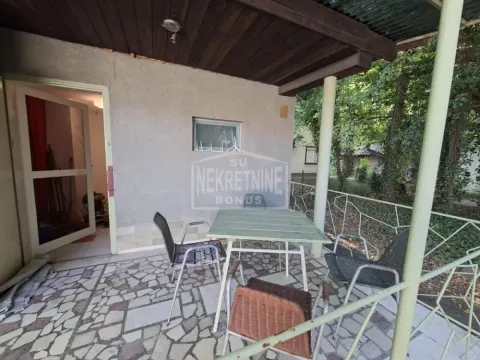 Natkrivena terasa sa stolom i stolicama ispred ulaza u kuću. - image 5