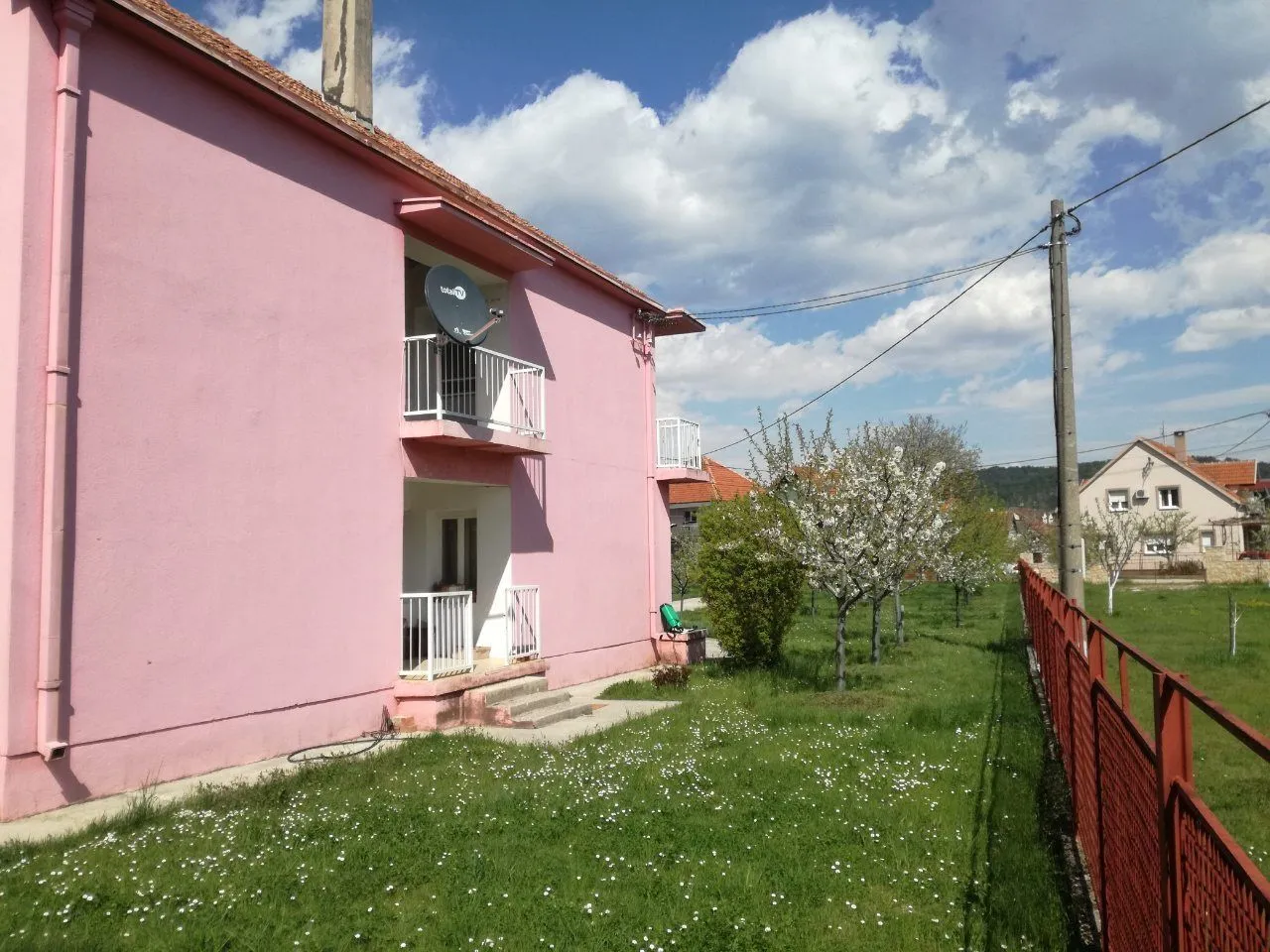 Vanjski izgled roze kuće sa dvorištem i zelenom travom.
