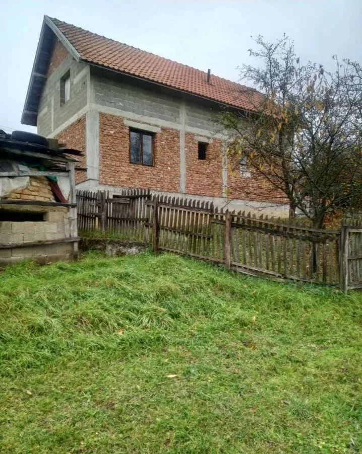 Pogled na spoljašnjost kuće sa dvorištem i ogradom.