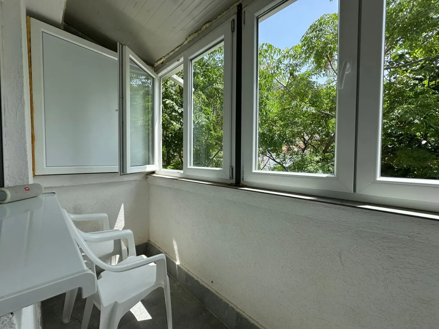 Zastakljeni balkon sa bijelim baštenskim namještajem i pogledom na zelenilo.