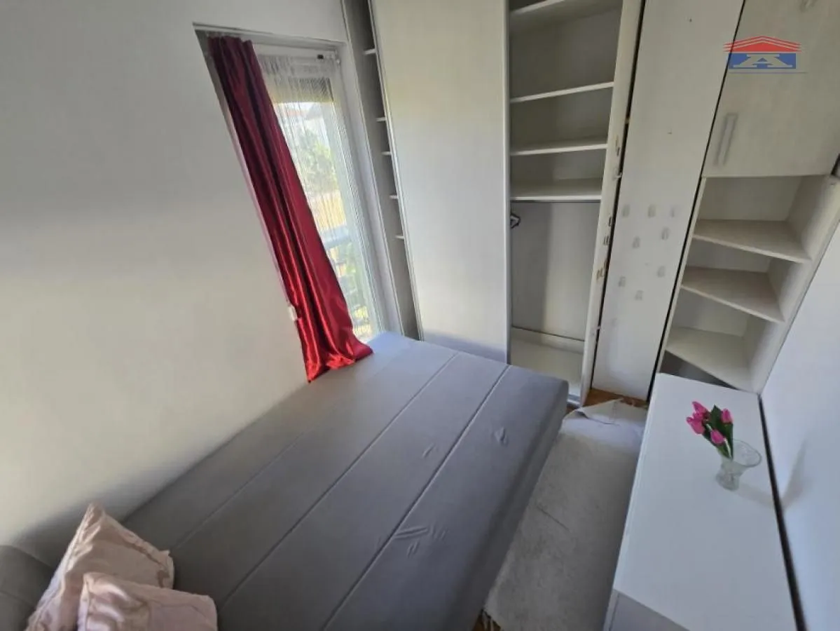 Manja spavaća soba sa krevetom, ugradnim plakarom i prozorom.