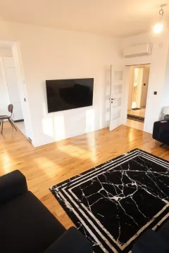 Dnevna soba sa drvenim podom, televizorom na zidu i tepihom. - image 3
