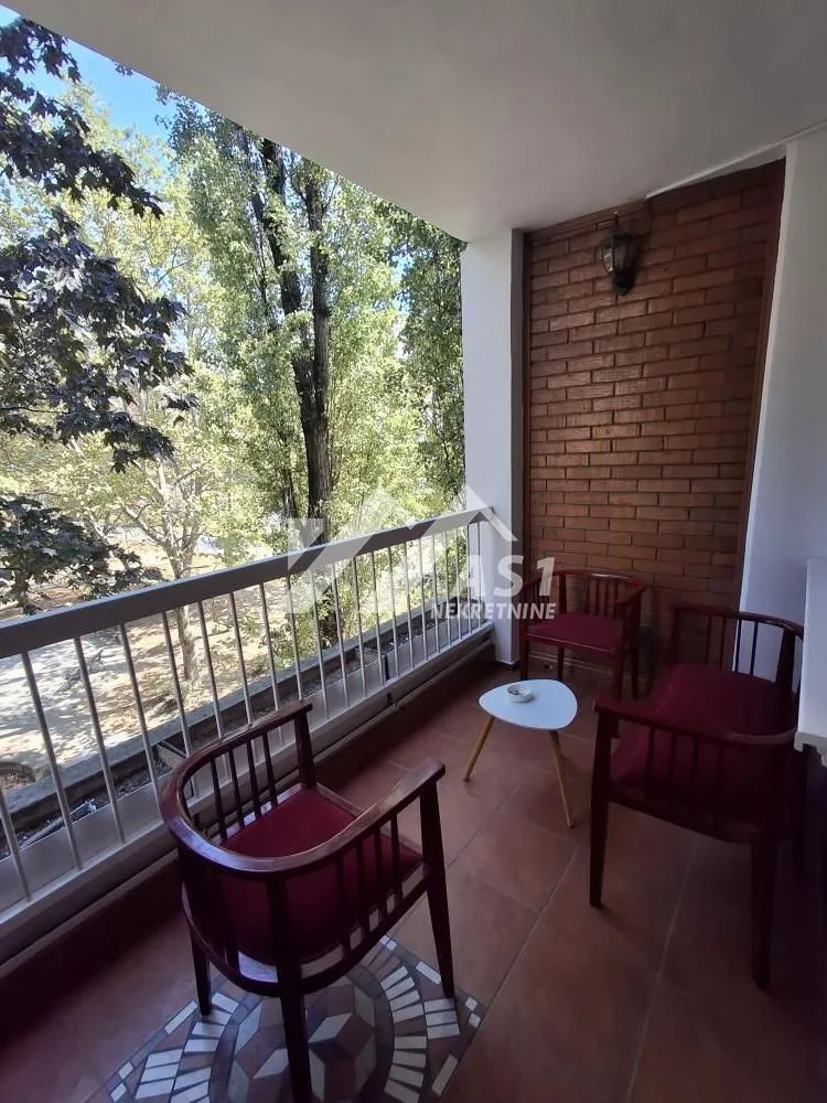 Natkriveni balkon sa garniturom za sedenje i pogledom na zelenilo.