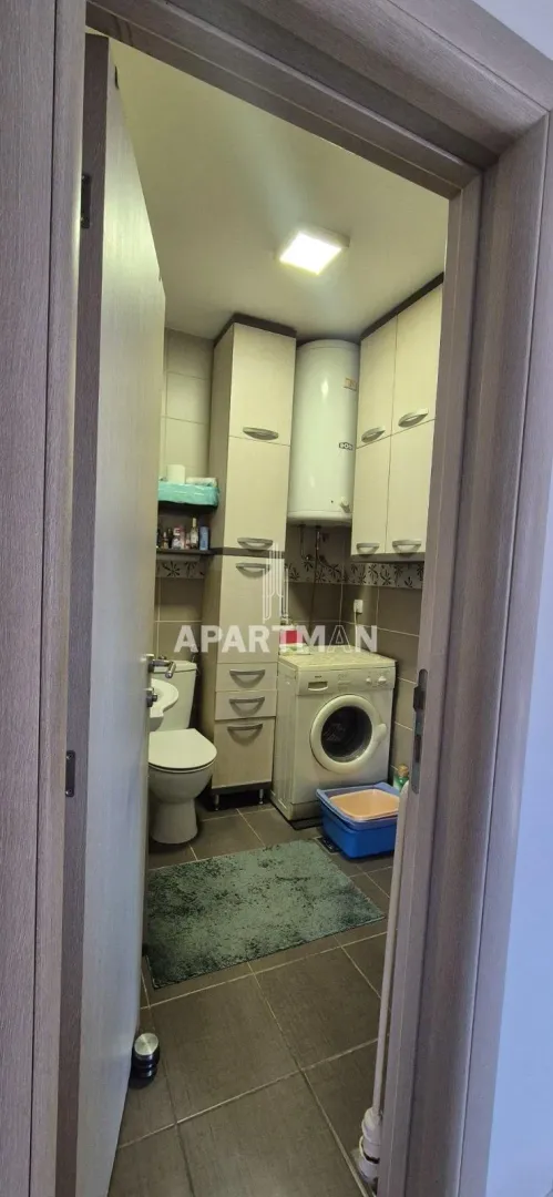 View through the doorway into the bathroom with a toilet, washing machine, and cabinets.