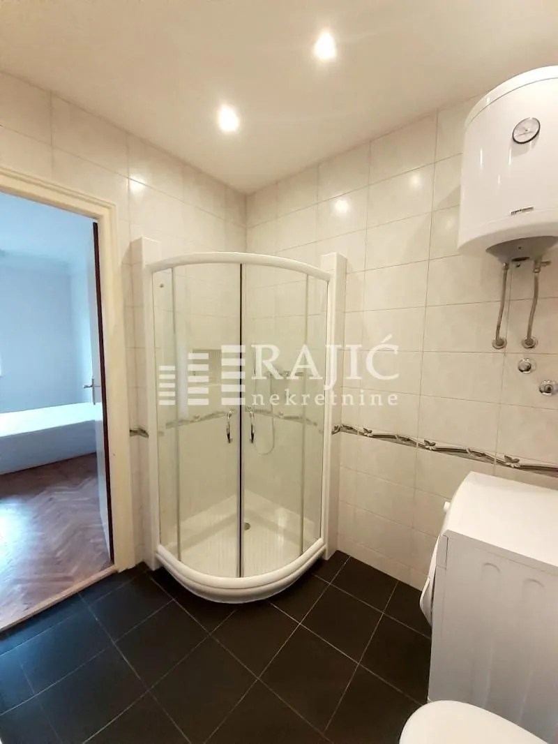 Smaller bathroom with a shower cabin, water heater, and ceramic tiles.