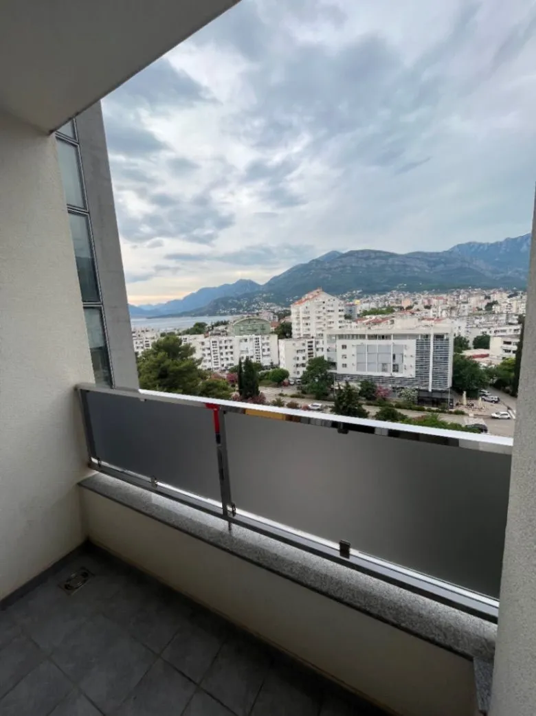 Manji popločani balkon sa staklenom ogradom i pogledom na grad i planine.