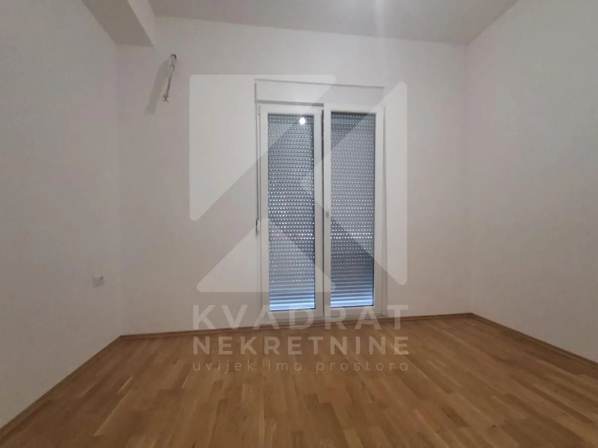 Empty unfurnished room with parquet flooring and balcony doors with roller shutters.
