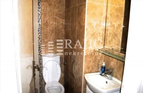 Smaller bathroom with a toilet, washbasin, and brown ceramic tiles. - image 13