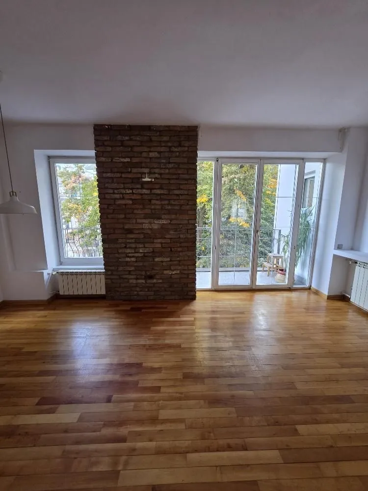 Empty living room with wooden flooring, a brick pillar, and access to the terrace.