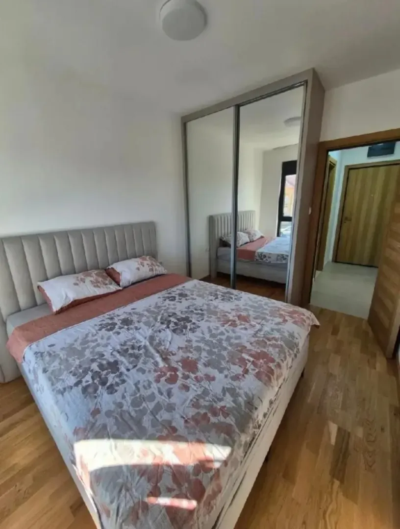 Namještena spavaća soba sa bračnim krevetom i ugradnim plakarom sa ogledalom.