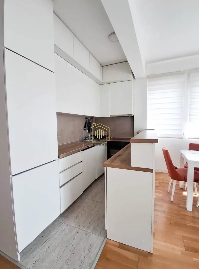 Moderna bijela kuhinja sa drvenim radnim površinama i trpezarijskim dijelom.