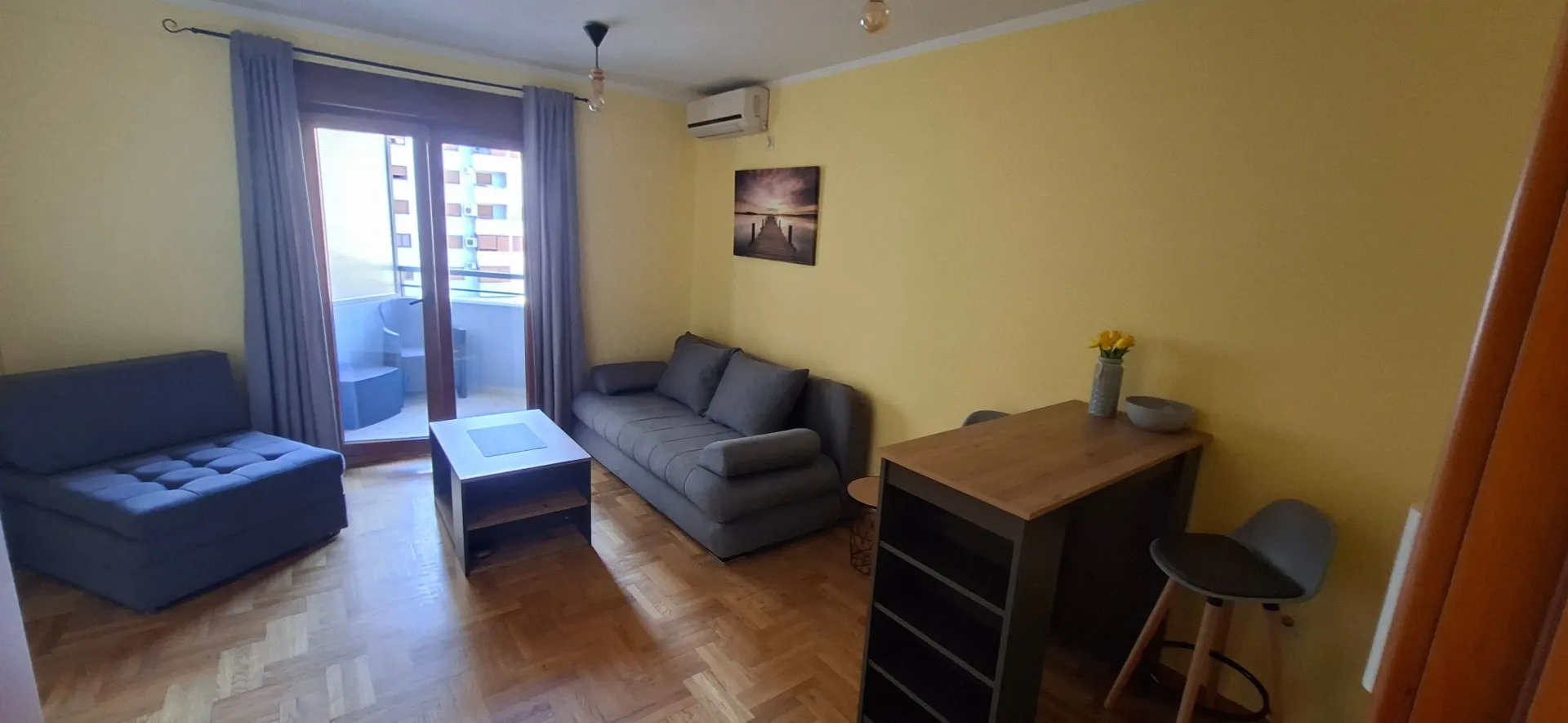 Living room with a sofa set, dining table, and balcony access.