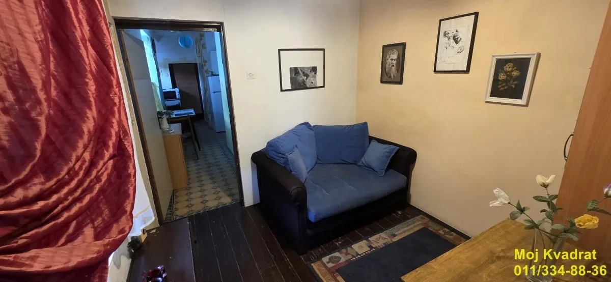 Manja dnevna soba sa plavom foteljom i slikama na zidu.