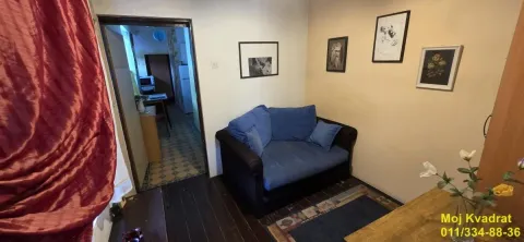 Manja dnevna soba sa plavom foteljom i slikama na zidu. - image 3