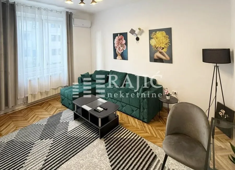 Furnished living room with a green sofa, rug, and decorative paintings on the wall.