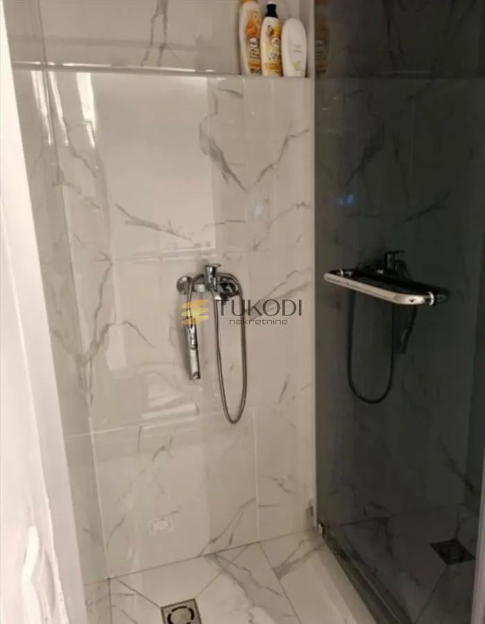 Walk-in shower enclosure with marble-look tiles and modern fixtures.