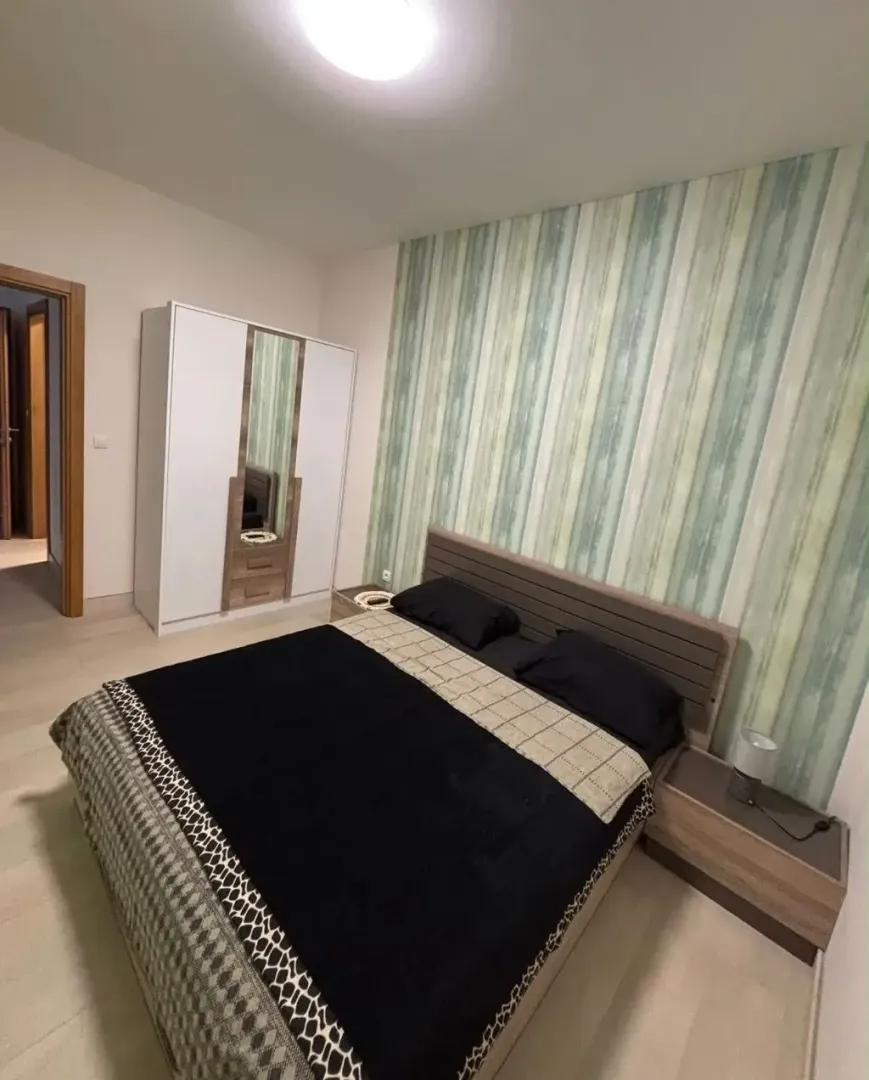 Spavaća soba sa bračnim krevetom, garderoberom i dekorativnim tapetama na zidu.