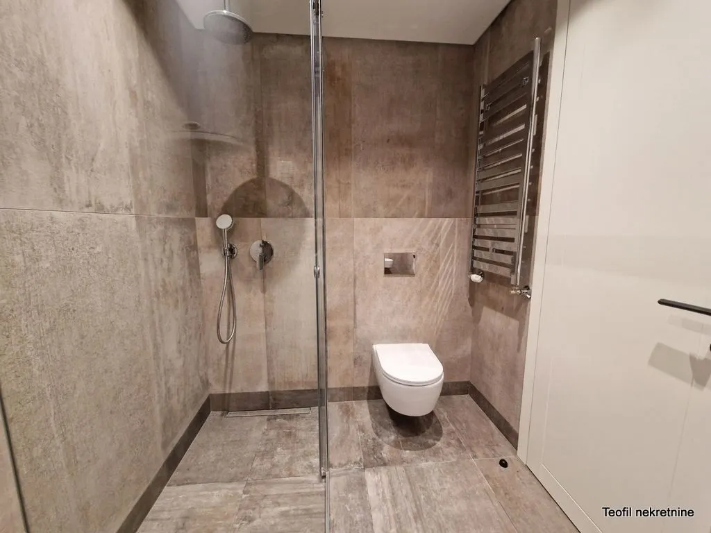 Moderno kupatilo sa tuš kabinom obloženom staklom i ugradnom šoljom.