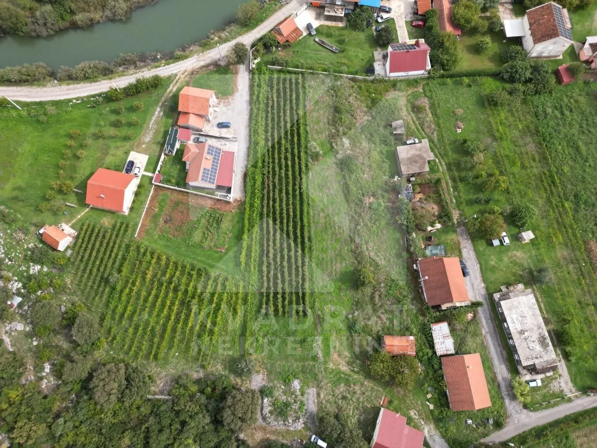 Pogled iz vazduha na imanje sa kućama, voćnjacima i rijekom u blizini.