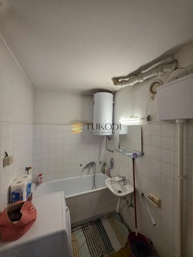 Starije opremljeno kupatilo sa kadom, lavaboom i bojlerom.