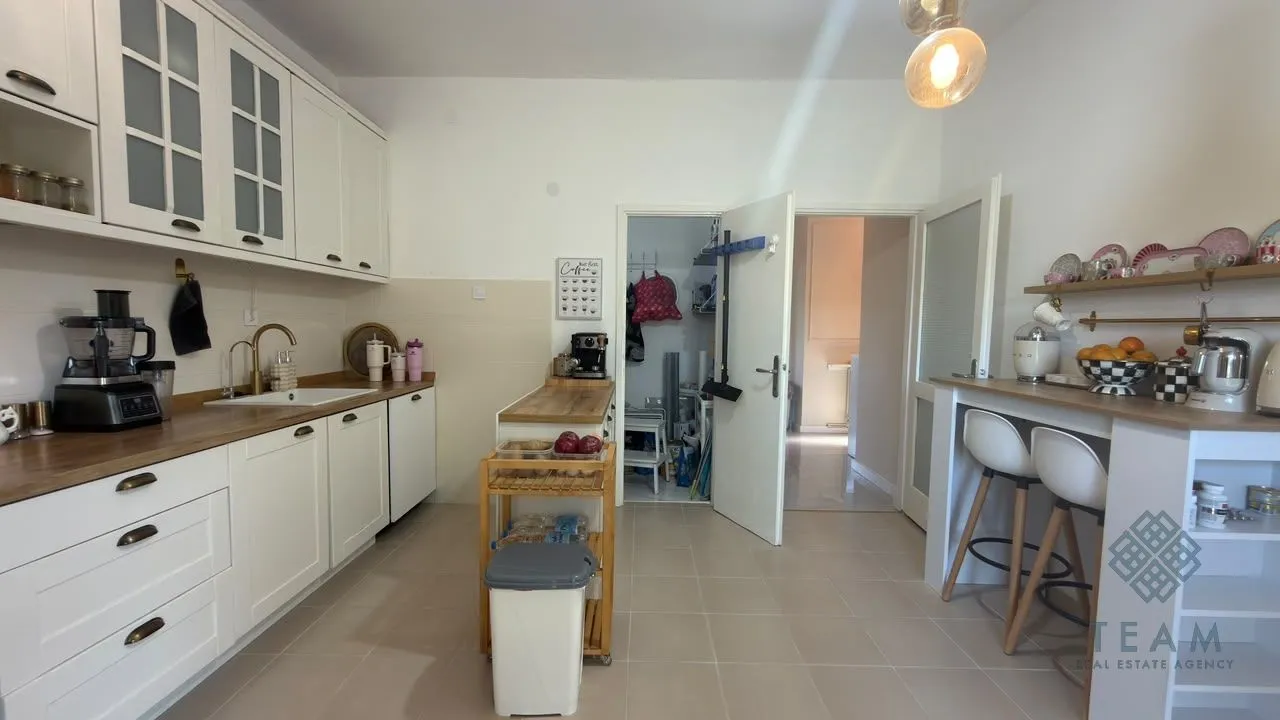 Bijela kuhinja sa drvenim radnim površinama, ostrvom i šankom za sjedenje.