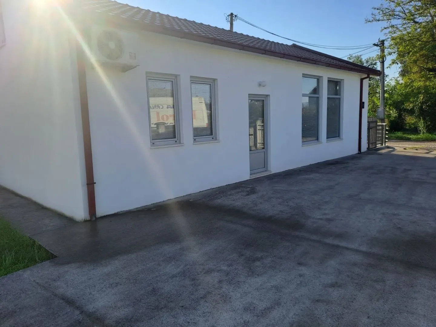 Pogled na spoljašnjost prizemne bijele kuće sa betonskim dvorištem.
