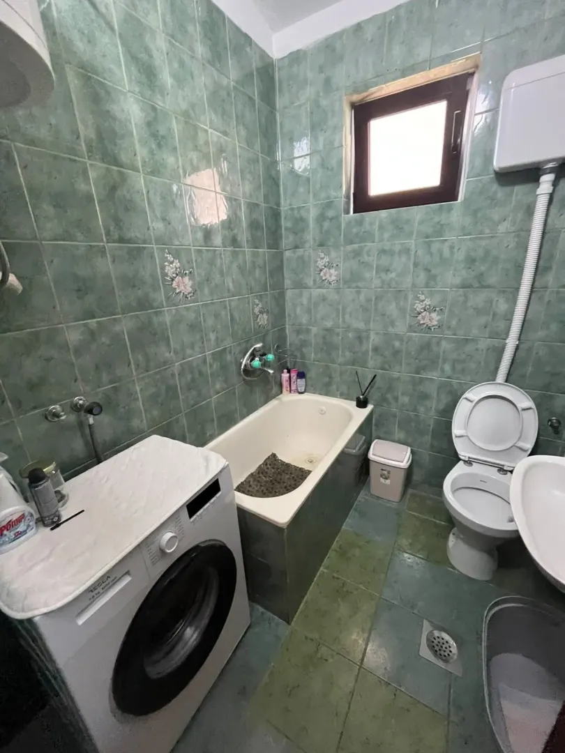 Kupatilo sa kadom, toaletom, umivaonikom i veš mašinom obloženo zelenim pločicama.