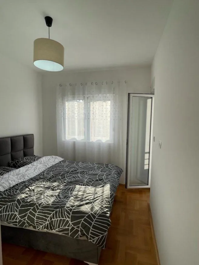 Bright bedroom with a double bed, parquet flooring, and a window.