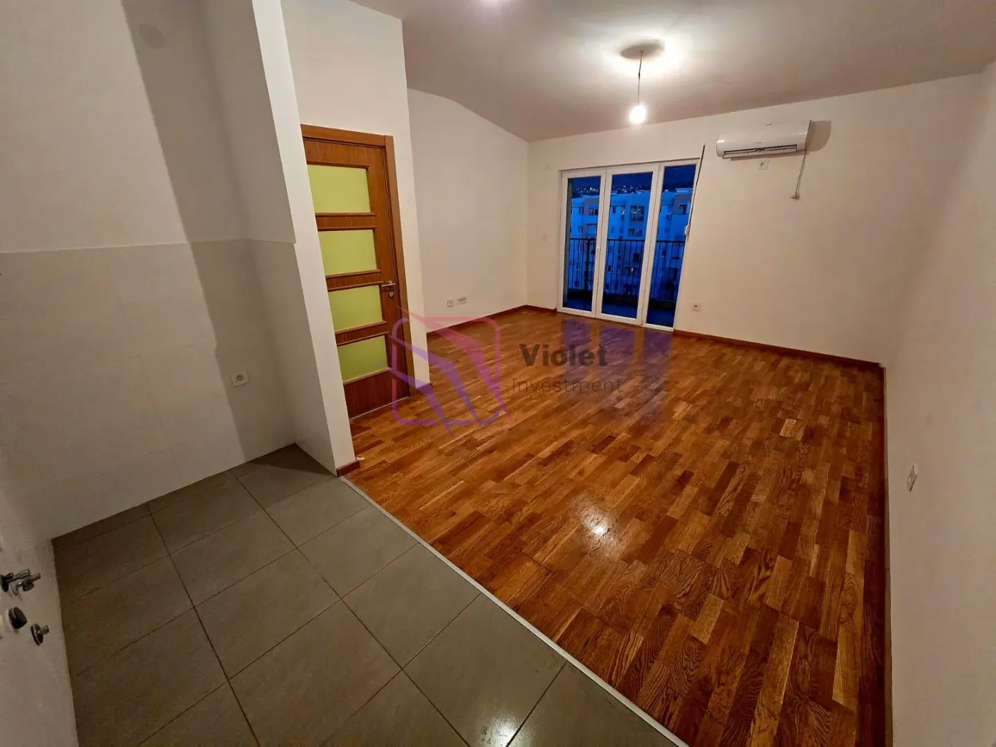 Prazna dnevna soba sa drvenim podom i balkonskim vratima.