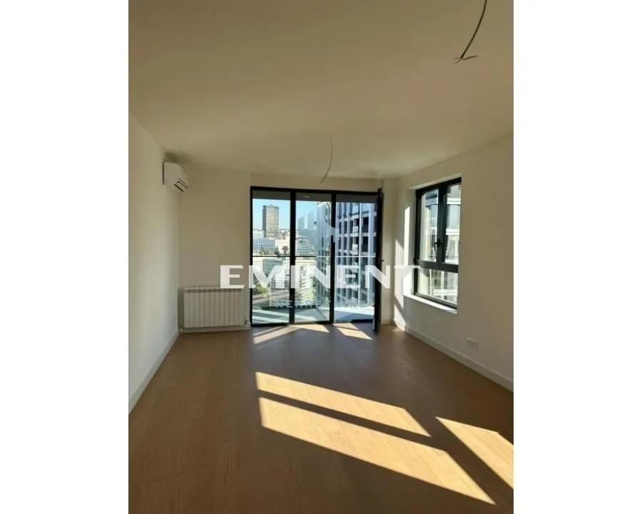 Empty room with wooden flooring, large windows, and balcony access.
