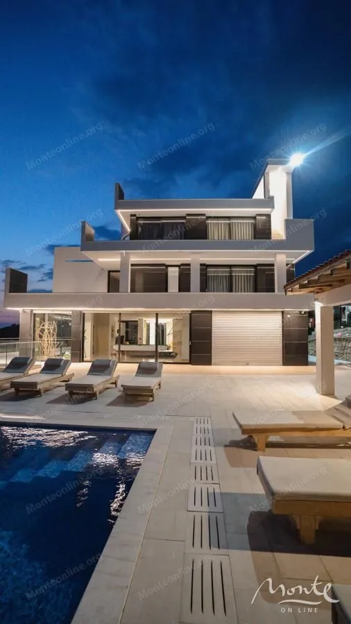 View of the villa with a swimming pool and sun loungers in the courtyard at night.