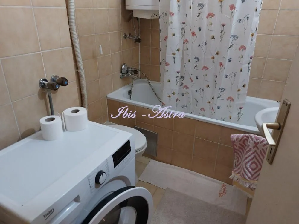 Small bathroom with a bathtub, washing machine, and beige tiles.