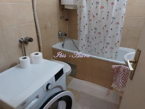 Small bathroom with a bathtub, washing machine, and beige tiles. - image 9
